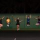 Group of teenagers jumping in celebration on an outdoor tennis court at night.