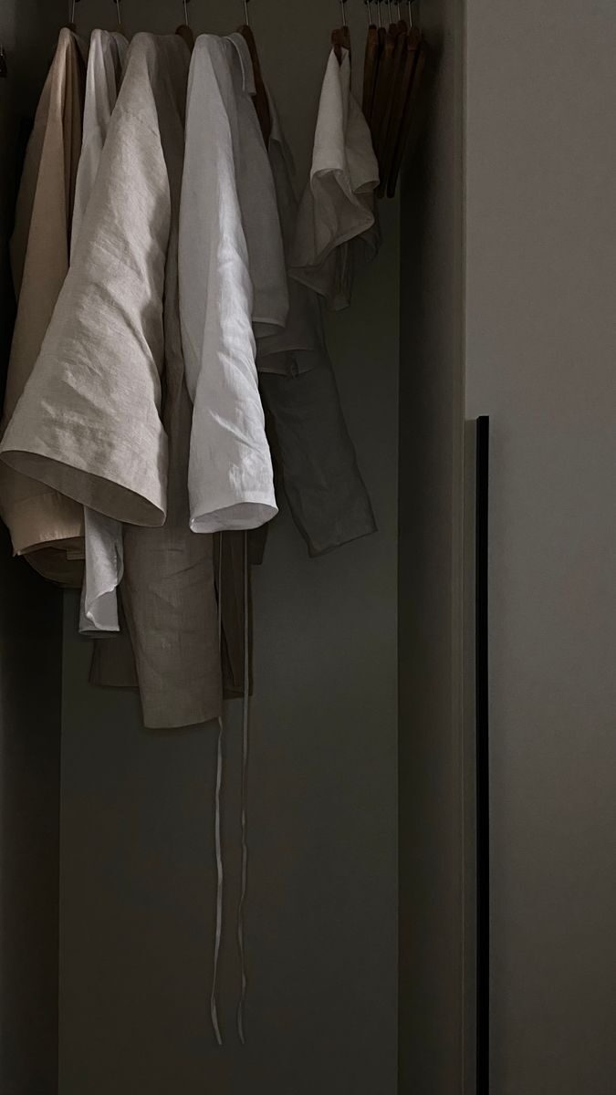 Linen clothes hanging on wooden hangers in a softly lit closet, showcasing neutral tones and textures.