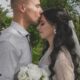 A groom kisses his bride's forehead during their outdoor wedding ceremony.
