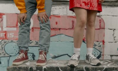 Two people in stylish streetwear against a graffiti backdrop, highlighting urban fashion with jeans and sneakers.