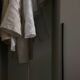 Linen clothes hanging on wooden hangers in a softly lit closet, showcasing neutral tones and textures.