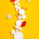 Colorful pills and tablets scattered on a vivid yellow background, symbolizing medicine and health.