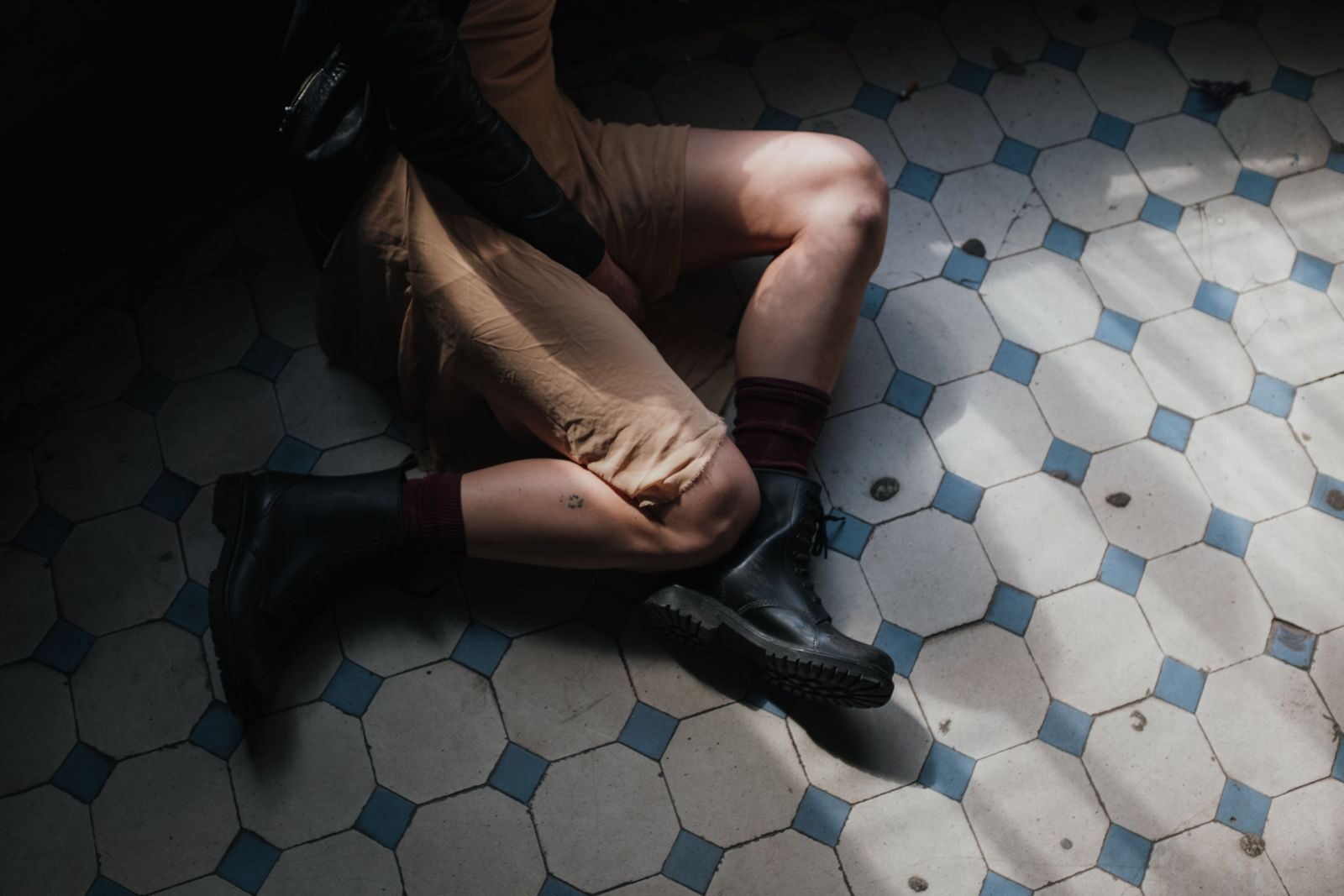 An artistic shot of a woman sitting on a vintage patterned tiled floor, showcasing fashion and style.