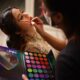 A makeup artist applies vibrant eyeshadow to a client's eyelids using a diverse palette.