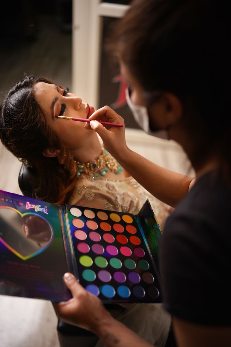 A makeup artist applies vibrant eyeshadow to a client's eyelids using a diverse palette.