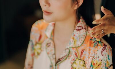 A woman with long hair sitting indoors, wearing a colorful blouse, getting her hair styled.