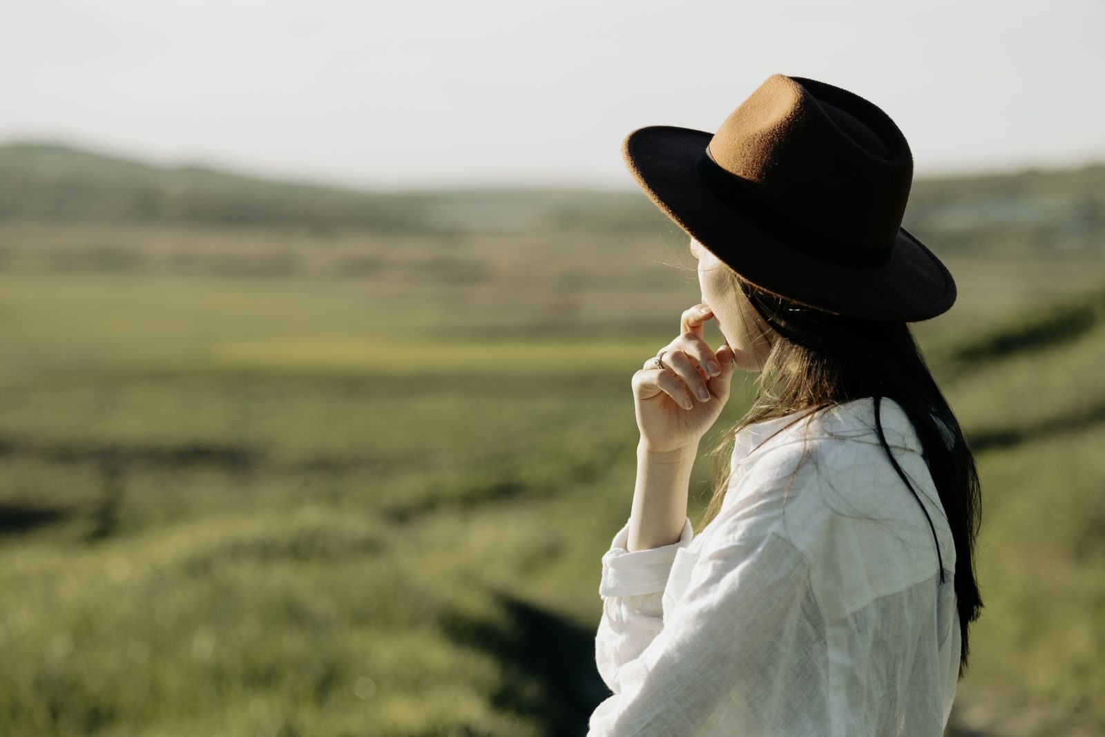 Woman in a hat gazes over the picturesque countryside under a sunny sky.