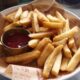 A plate of golden, crispy French fries served with a side of ketchup.