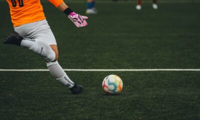 A soccer goalkeeper prepares to kick a colorful ball on a grass field.