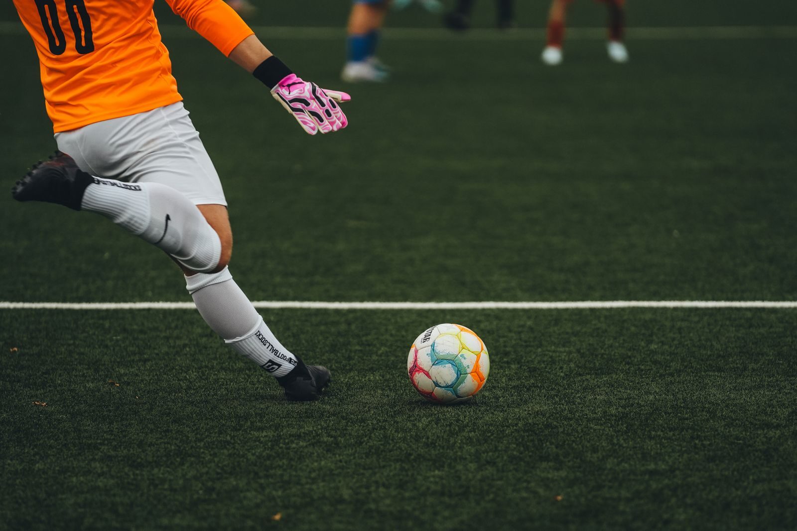 A soccer goalkeeper prepares to kick a colorful ball on a grass field.