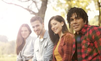 A diverse group of friends sitting outdoors, smiling and enjoying a sunny day.