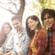A diverse group of friends sitting outdoors, smiling and enjoying a sunny day.