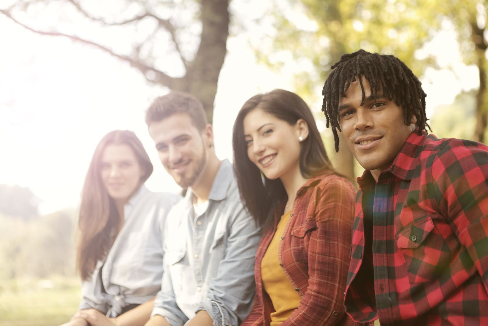 A diverse group of friends sitting outdoors, smiling and enjoying a sunny day.