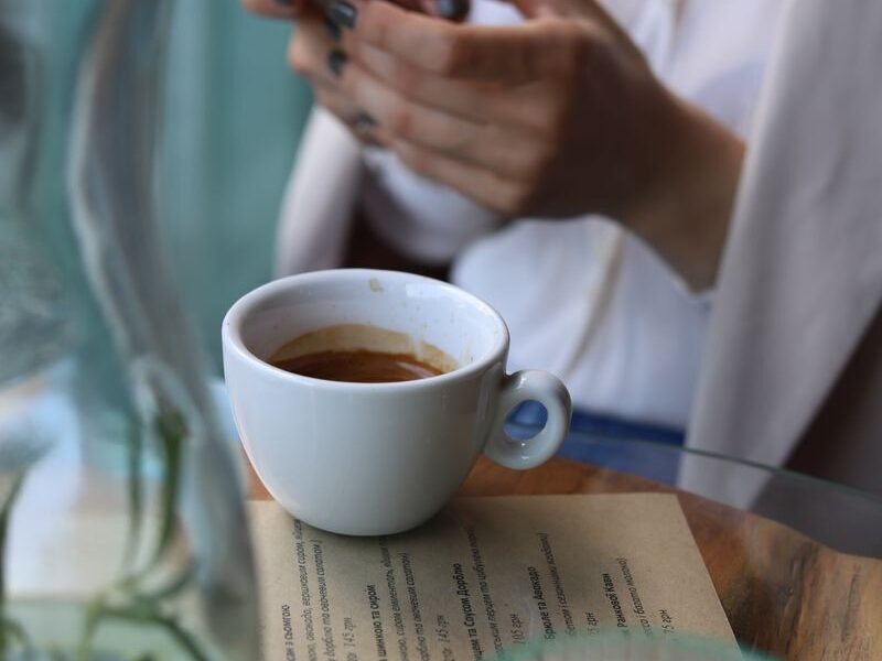 Woman with a coffee and smartphone at a cafe table, creating a cozy and modern ambiance.