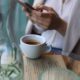 Woman with a coffee and smartphone at a cafe table, creating a cozy and modern ambiance.