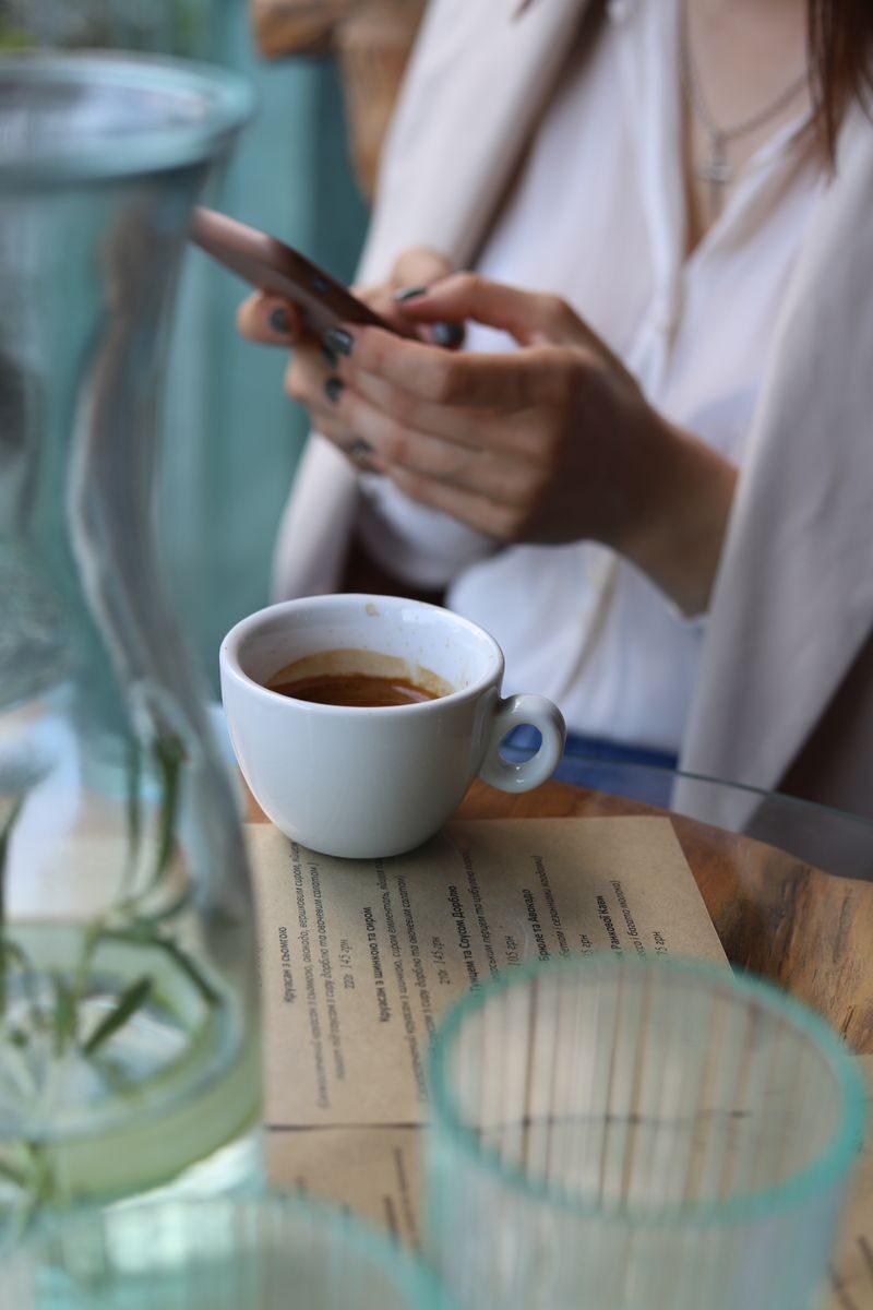 Woman with a coffee and smartphone at a cafe table, creating a cozy and modern ambiance.