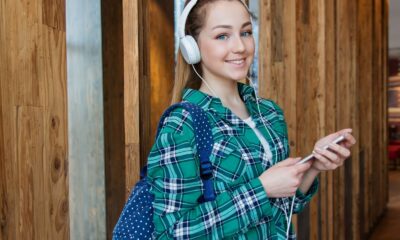 Smiling young woman wearing headphones and holding a smartphone indoors.