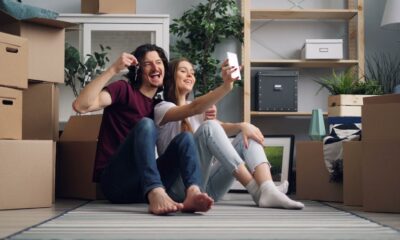 A joyful couple sitting amidst boxes, taking a selfie in their new home.