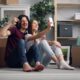 A joyful couple sitting amidst boxes, taking a selfie in their new home.