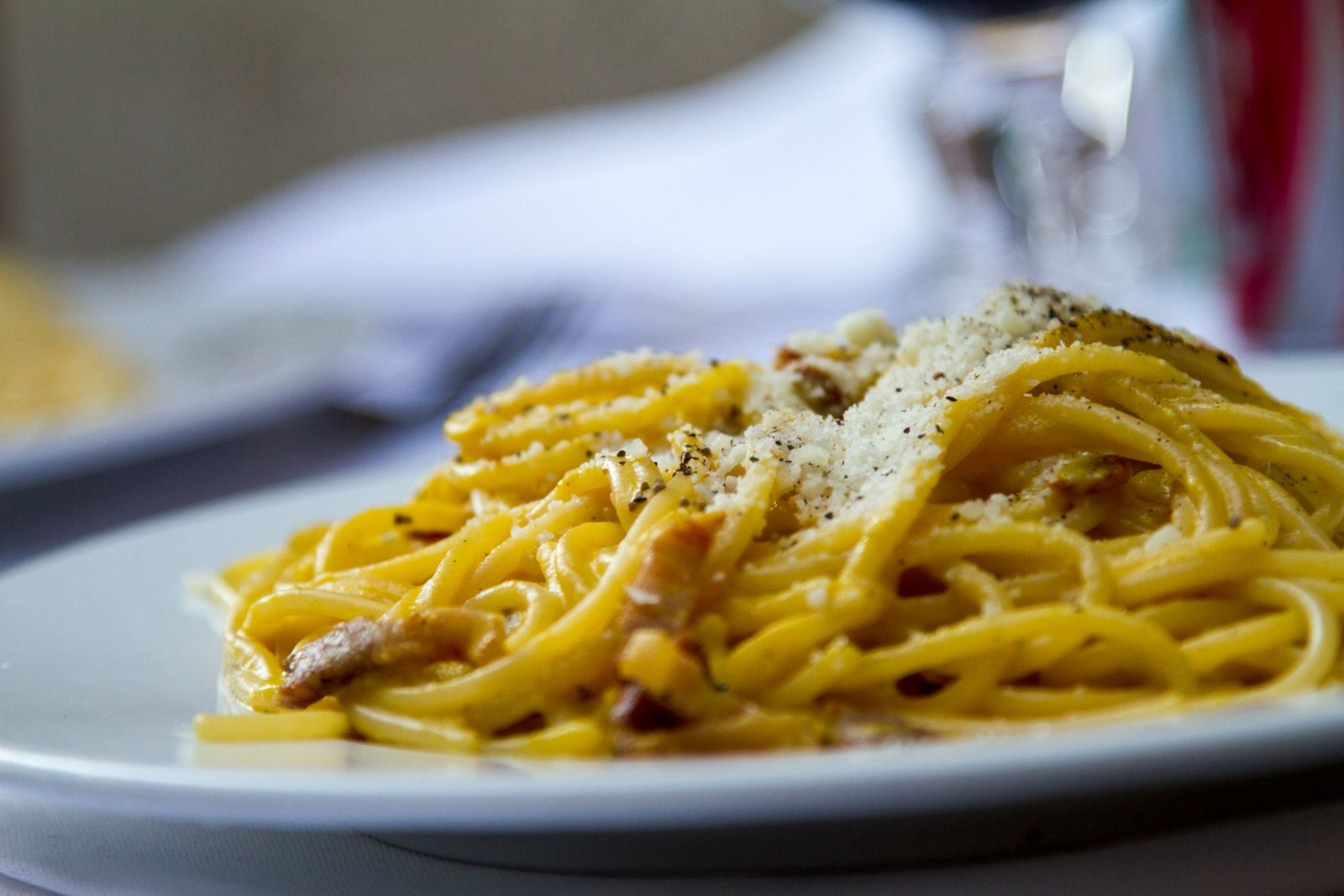 Close-up of spaghetti carbonara topped with grated Parmesan cheese on a plate, perfect for Italian cuisine lovers.